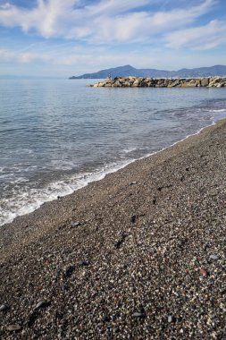 Güneşli bir günde kumsalda çakıl taşları ve arka planda kayalıklar vardı.
