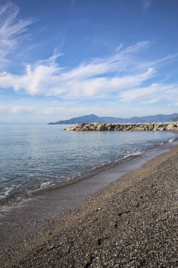 Güneşli bir günde kumsalda çakıl taşları ve arka planda kayalıklar vardı.