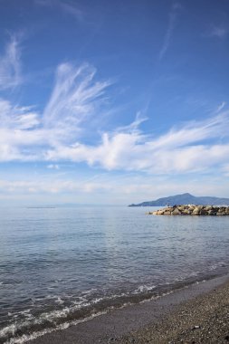 Güneşli bir günde kumsalda çakıl taşları ve arka planda kayalıklar vardı.