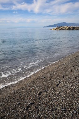 Güneşli bir günde kumsalda çakıl taşları ve arka planda kayalıklar vardı.