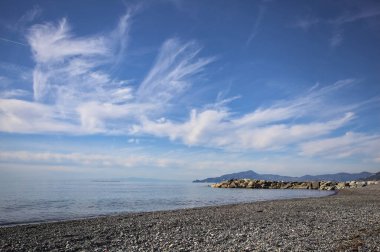 Güneşli bir günde kumsalda çakıl taşları ve arka planda kayalıklar vardı.