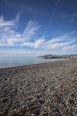 Güneşli bir günde kumsalda çakıl taşları ve arka planda kayalıklar vardı.