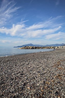Güneşli bir günde kumsalda çakıl taşları ve arka planda kayalıklar vardı.
