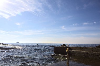 Güneşli bir günde, deniz kenarındaki su dalgalarıyla birlikte su seviyesindeki kayaların yanına beton demirleme yeri inşa edildi.