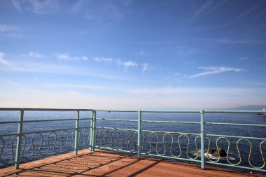 # Gök mavisi bir korkulukla # # Altında deniz olan bir uçurum # # Ve güneşli bir günde # # bir balkonda sarı bir tatil köyü binası #