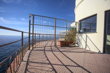 Güneşli bir günde ufka kadar uzanan bir uçurumun üzerindeki kapalı bir restoranın panoramik terasına çıkan bir binanın çitindeki kapalı kapı.