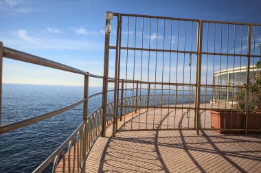 Güneşli bir günde ufka kadar uzanan bir uçurumun üzerindeki kapalı bir restoranın panoramik terasına çıkan bir binanın çitindeki kapalı kapı.