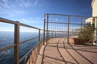 Güneşli bir günde ufka kadar uzanan bir uçurumun üzerindeki kapalı bir restoranın panoramik terasına çıkan bir binanın çitindeki kapalı kapı.