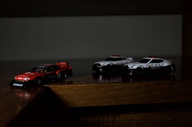 Cenova, İtalya - 20th NOVEMBER 2025 - Nissan Skyline Turbo Super Silueti 'nin kırmızı ve siyah yarış kıyafetleri içindeki Takara Tomi kopyaları Nissan Skyline GT-R R34 ve Japon polis üniformalarındaki Nissan Fairlady 350Z al