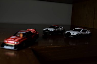 Cenova, İtalya - 20th NOVEMBER 2025 - Nissan Skyline Turbo Super Silueti 'nin kırmızı ve siyah yarış kıyafetleri içindeki Takara Tomi kopyaları Nissan Skyline GT-R R34 ve Japon polis üniformalarındaki Nissan Fairlady 350Z al