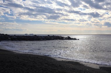 Denizin dalgaları bir uçurumun kayalıklarına çarpıyor. Güneş ışığı yukarıdan görünen suya vuruyor.