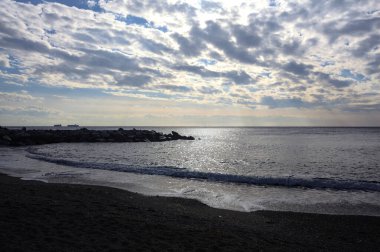 Denizin dalgaları bir uçurumun kayalıklarına çarpıyor. Güneş ışığı yukarıdan görünen suya vuruyor.