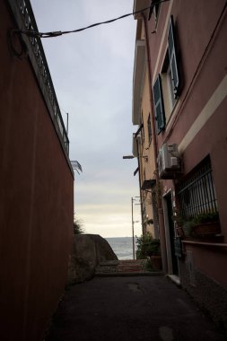 Ufukta bulutlu bir gün batımına kadar uzanan denizleri çerçeveleyen evler arasında dar bir geçit.