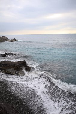 Gün batımında, deniz kıyısında ve bir uçurumun kayalıklarında ufka doğru uzanan deniz dalgaları.