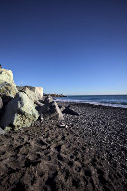 Foreshore by the sea on a sunny day with clear sky framed by rocks by the edge of a beach