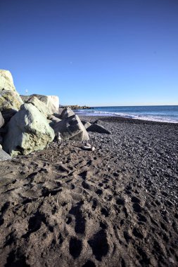 Foreshore by the sea on a sunny day with clear sky framed by rocks by the edge of a beach