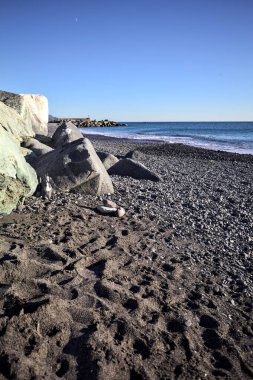 Foreshore by the sea on a sunny day with clear sky framed by rocks by the edge of a beach