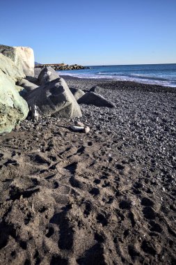 Foreshore by the sea on a sunny day with clear sky framed by rocks by the edge of a beach