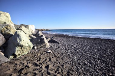 Foreshore by the sea on a sunny day with clear sky framed by rocks by the edge of a beach