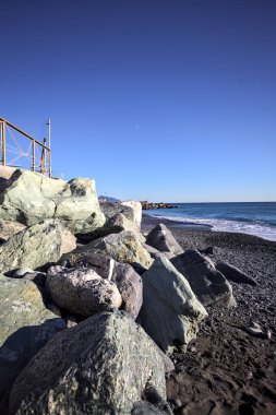 Foreshore by the sea on a sunny day with clear sky framed by rocks by the edge of a beach