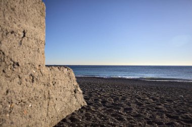 Foreshore of a beach at sunset framed by the portion of a concrete wall