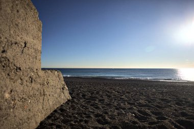 Foreshore of a beach at sunset framed by the portion of a concrete wall