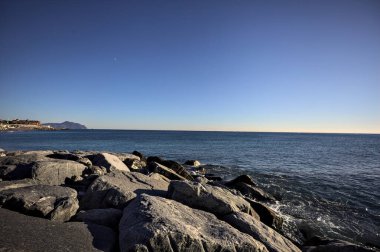 Küçük bir körfezden görünen ve dalgakıran kayaları tarafından çerçevelenen binalar ve uçurumun kenarındaki bir çıkıntının ucu.