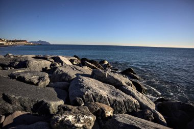 Küçük bir körfezden görünen ve dalgakıran kayaları tarafından çerçevelenen binalar ve uçurumun kenarındaki bir çıkıntının ucu.