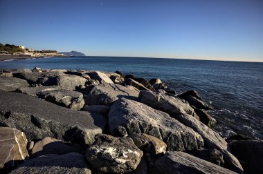 Küçük bir körfezden görünen ve dalgakıran kayaları tarafından çerçevelenen binalar ve uçurumun kenarındaki bir çıkıntının ucu.