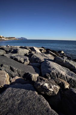 Küçük bir körfezden görünen ve dalgakıran kayaları tarafından çerçevelenen binalar ve uçurumun kenarındaki bir çıkıntının ucu.