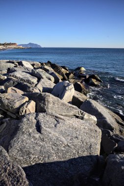 Küçük bir körfezden görünen ve dalgakıran kayaları tarafından çerçevelenen binalar ve uçurumun kenarındaki bir çıkıntının ucu.