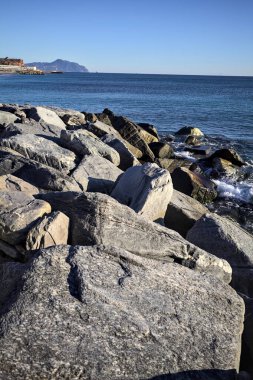 Küçük bir körfezden görünen ve dalgakıran kayaları tarafından çerçevelenen binalar ve uçurumun kenarındaki bir çıkıntının ucu.