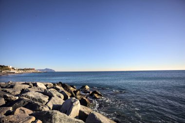 Küçük bir körfezden görünen ve dalgakıran kayaları tarafından çerçevelenen binalar ve uçurumun kenarındaki bir çıkıntının ucu.