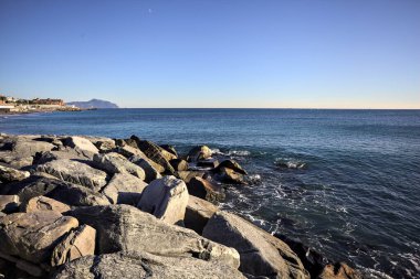 Küçük bir körfezden görünen ve dalgakıran kayaları tarafından çerçevelenen binalar ve uçurumun kenarındaki bir çıkıntının ucu.