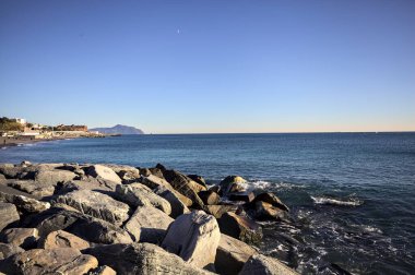 Küçük bir körfezden görünen ve dalgakıran kayaları tarafından çerçevelenen binalar ve uçurumun kenarındaki bir çıkıntının ucu.