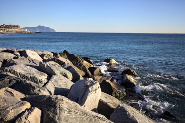 Küçük bir körfezden görünen ve dalgakıran kayaları tarafından çerçevelenen binalar ve uçurumun kenarındaki bir çıkıntının ucu.