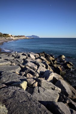 Küçük bir körfezden görünen ve dalgakıran kayaları tarafından çerçevelenen binalar ve uçurumun kenarındaki bir çıkıntının ucu.
