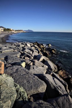 Küçük bir körfezden görünen ve dalgakıran kayaları tarafından çerçevelenen binalar ve uçurumun kenarındaki bir çıkıntının ucu.