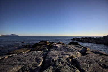 Gün batımında bir uçurumun kayaları su seviyesinde görülür ve deniz Horizon 'a kadar uzanır.