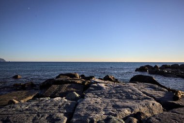 Gün batımında bir uçurumun kayaları su seviyesinde görülür ve deniz Horizon 'a kadar uzanır.
