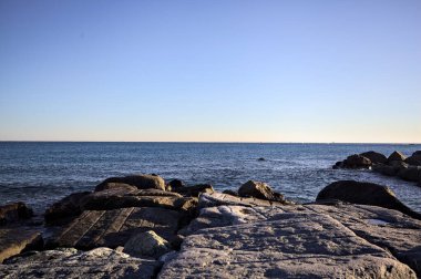 Gün batımında bir uçurumun kayaları su seviyesinde görülür ve deniz Horizon 'a kadar uzanır.