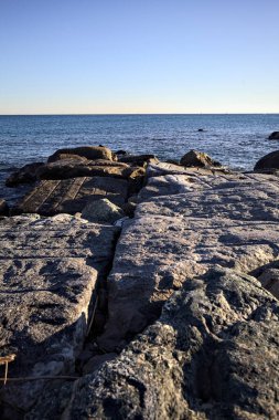 Rocks of a cliff at sunset seen at water level with the sea stretching to the Horizon