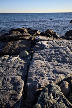 Rocks of a cliff at sunset seen at water level with the sea stretching to the Horizon