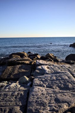 Rocks of a cliff at sunset seen at water level with the sea stretching to the Horizon