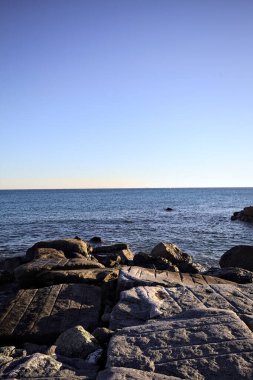 Rocks of a cliff at sunset seen at water level with the sea stretching to the Horizon