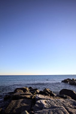 Rocks of a cliff at sunset seen at water level with the sea stretching to the Horizon