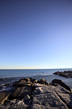 Rocks of a cliff at sunset seen at water level with the sea stretching to the Horizon