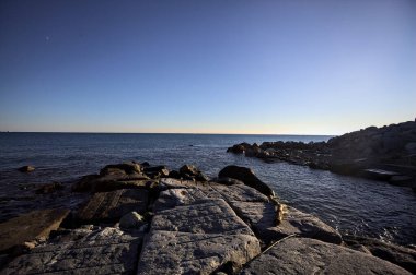 Gün batımında bir uçurumun kayaları su seviyesinde görülür ve deniz Horizon 'a kadar uzanır.