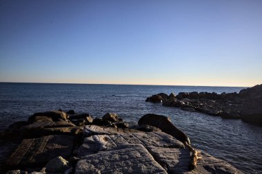Gün batımında bir uçurumun kayaları su seviyesinde görülür ve deniz Horizon 'a kadar uzanır.