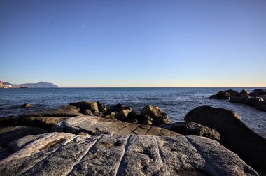 Küçük bir körfezden görünen ve dalgakıran kayaları tarafından çerçevelenen binalar ve uçurumun kenarındaki bir çıkıntının ucu.